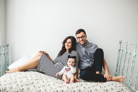 Happy young father, mother and cute baby boy lying on rustic bed