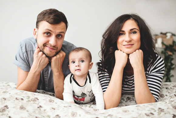 Happy young father mother and baby boy lying on bed